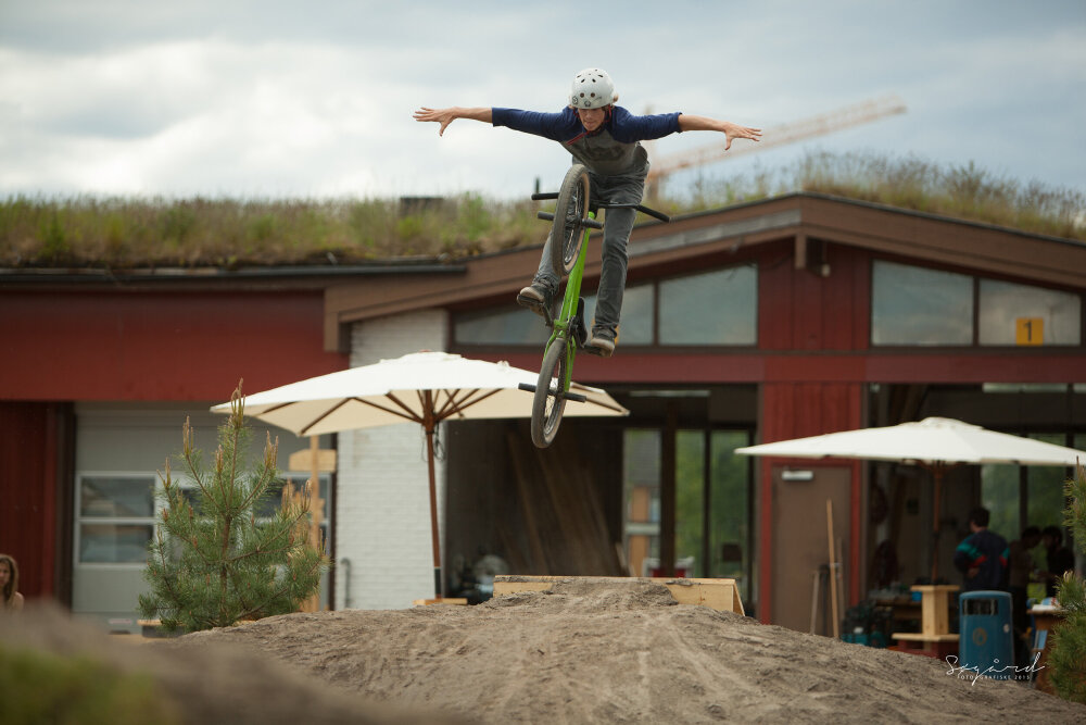 Gutt på sykkel hopper foran et hus med gress på taket
