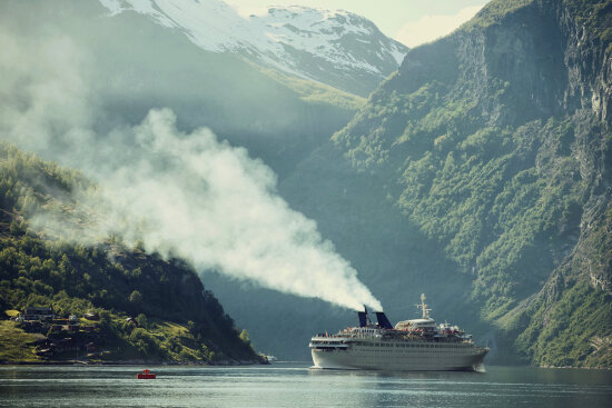 Cruiseskip i fjord med utslipp/røyk fra skorstein.