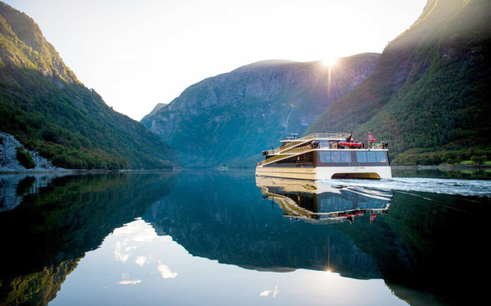 Båten Seasight på fjorden med høye fjell og solnedgang i bakgrunnen.