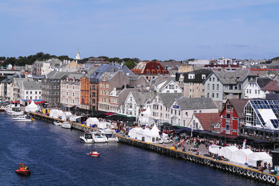 Haugesund brygge en solskinnsdag. Ser brygga, bygninger, kirkespir, blå himmel, fjord og båter