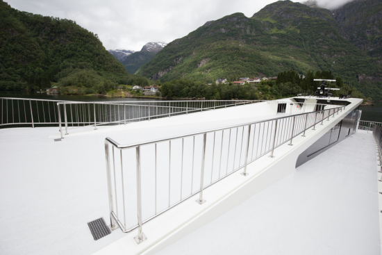 Detalj fra turistbåten som viser hvordan den er universelt tilgjengelig, slik at alle kan komme seg rundt på båten, uavhengig av funksjonsevne. I bakgrunnen åser og fjell og en flik av fjorden.