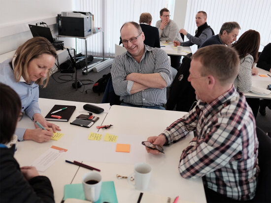 Workshop med mennesker som skriver på post-it-lapper samlet i grupper rundt bord.