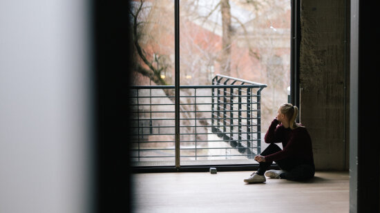 Jente sitter på gulvet og ser ut av et stort vindu