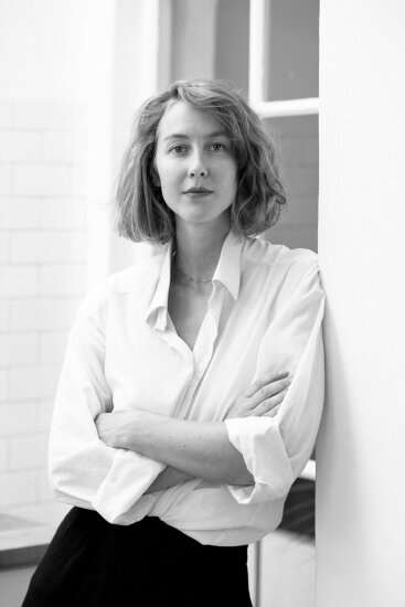 Kaja Solgaard Dahl står lent inn mot en vegg, armene i kors, et vindu i bakgrunnen. Bildet er i sort/hvitt.