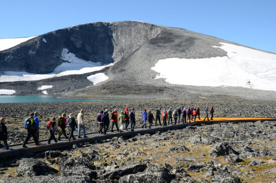 Mennesker går over klimaparken på åpningen av parken. Det er et stort fjell i bakgrunnen og blå himmel over dem.