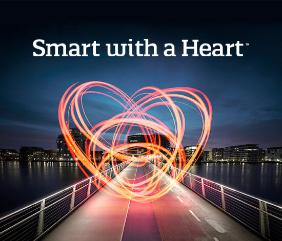 Tekst i bilde: «Smart with a Heart™». Bilde: bro over vann mot by om natten, med fyrverkeri-hjerte i sentrum.
