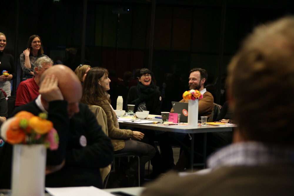 Workshop, leende deltagere rundt et bord 