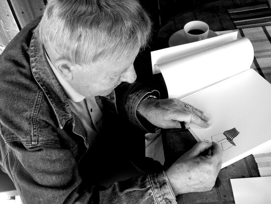 Bildet viser møbeldesigner Hans Brattrud som signerer en bok med bilde av stolen hans, Scandia Junior.