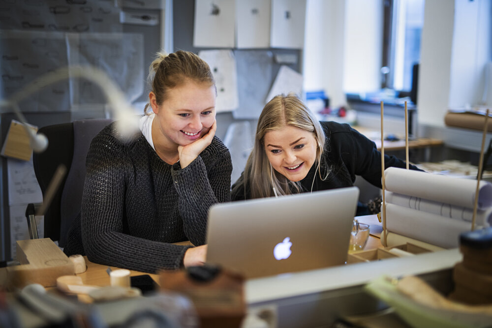 To jenter foran en bærbar datamaskin i et verksted-liknende miljø. 