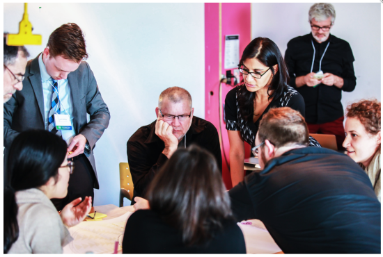 Mennesker stående og sittende rundt et bord på workshop.