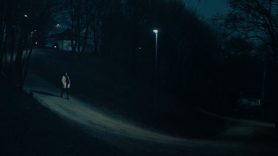 Kvinne går alene i mørk park.