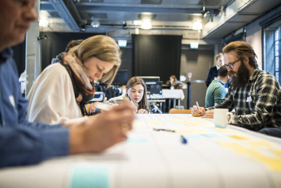 Mennesker tegner og skriver i workshop rundt bord.