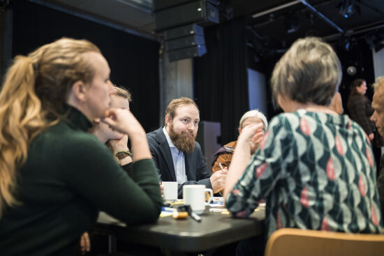 Mennesker diskuterer rundt bord i gruppe. Torkell Pettersen i midten.