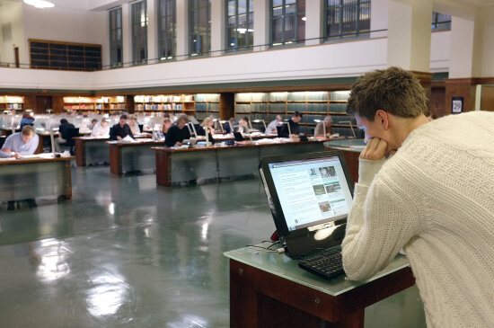 Lesesal på bibliotek. Til høyre foran i bildet leser en mann på en dataskjerm.