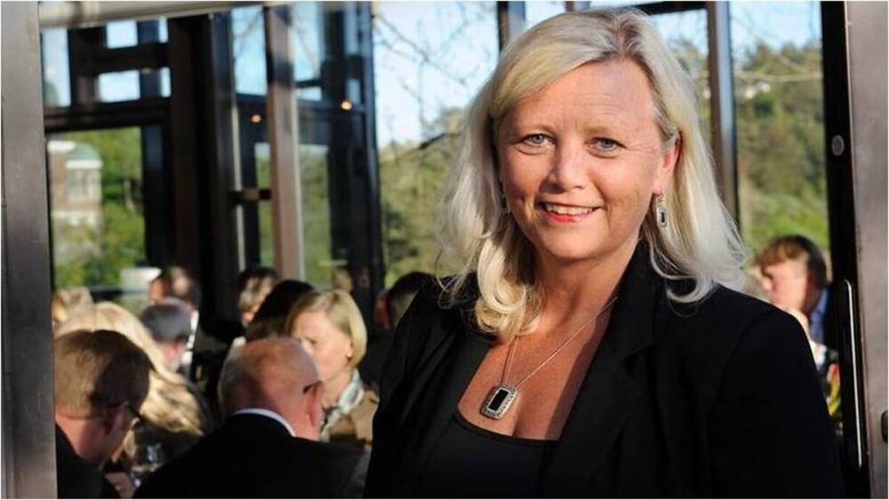 Bilde av dame, stående foran andre sittende mennesker.